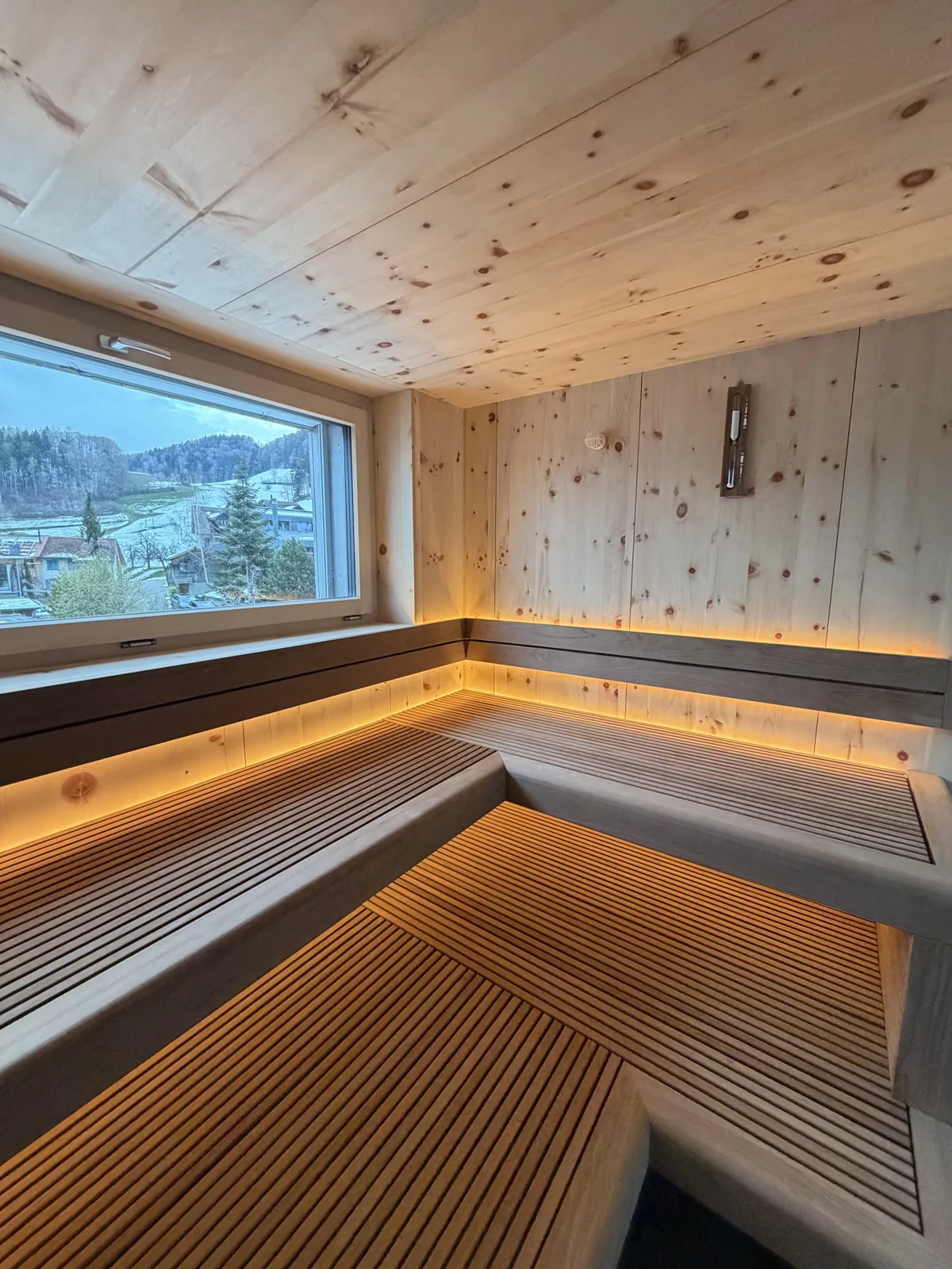 Sauna privé en pin cembro avec fenêtre et banquettes à éclairage indirect