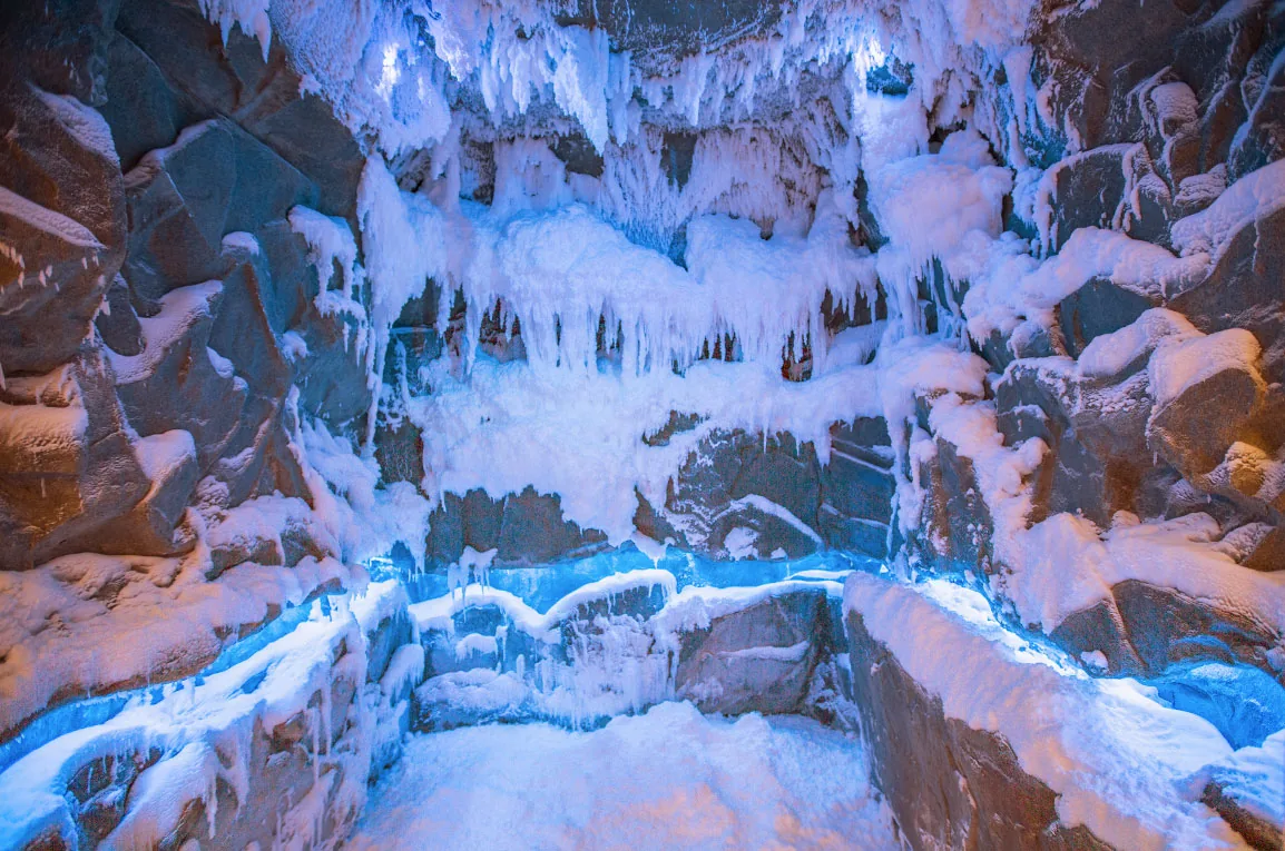 Snow room as an ice grotto with rock walls, icicles and blue-lit seating
